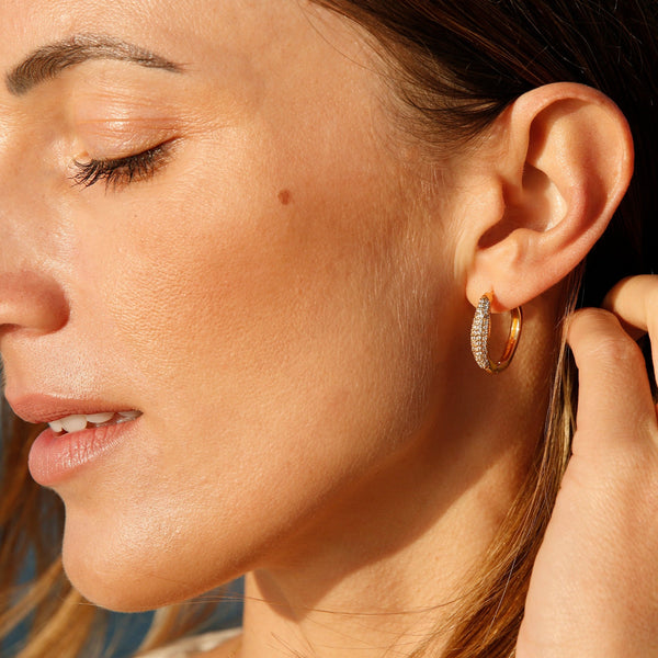A delicate yet glamorous pair of gold earrings. These golden hoop earrings feature pave set topaz stone and its subtle wave design imbues you with elegance and sparkle. Team these gold earrings with the matching Athena Ear Cuff and an essential gold necklace from our collection.