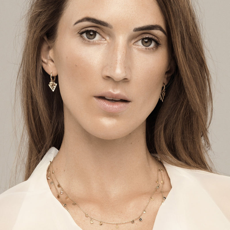 This 14 karat gold necklace features five white bezel-set sapphire stones with dangling gold triangle charms.